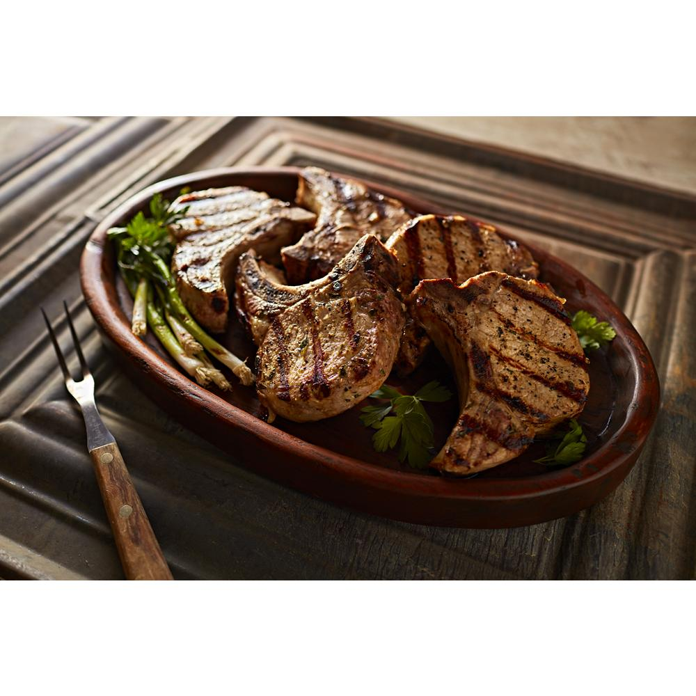 Grilled pork chops with sear marks served on a rustic tray with fresh herbs and green onions, KitchenAid kitchenware