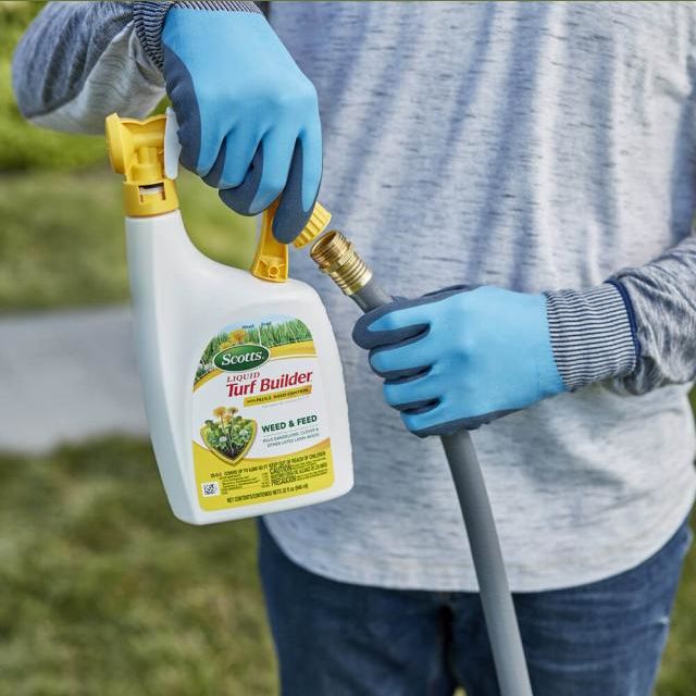 Person wearing blue gloves attaching hose to yellow and white liquid turf builder sprayer for lawn care tasks