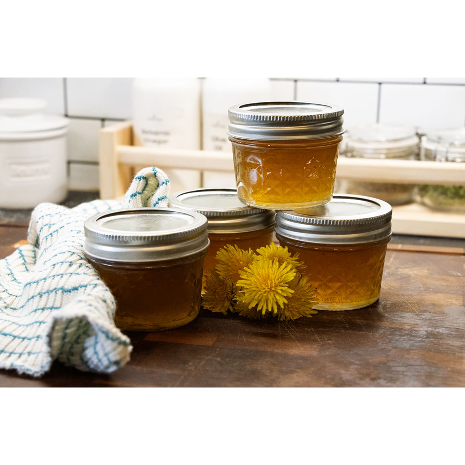 Four small clear glass jars with silver lids filled with homemade jam on wooden kitchen counter
