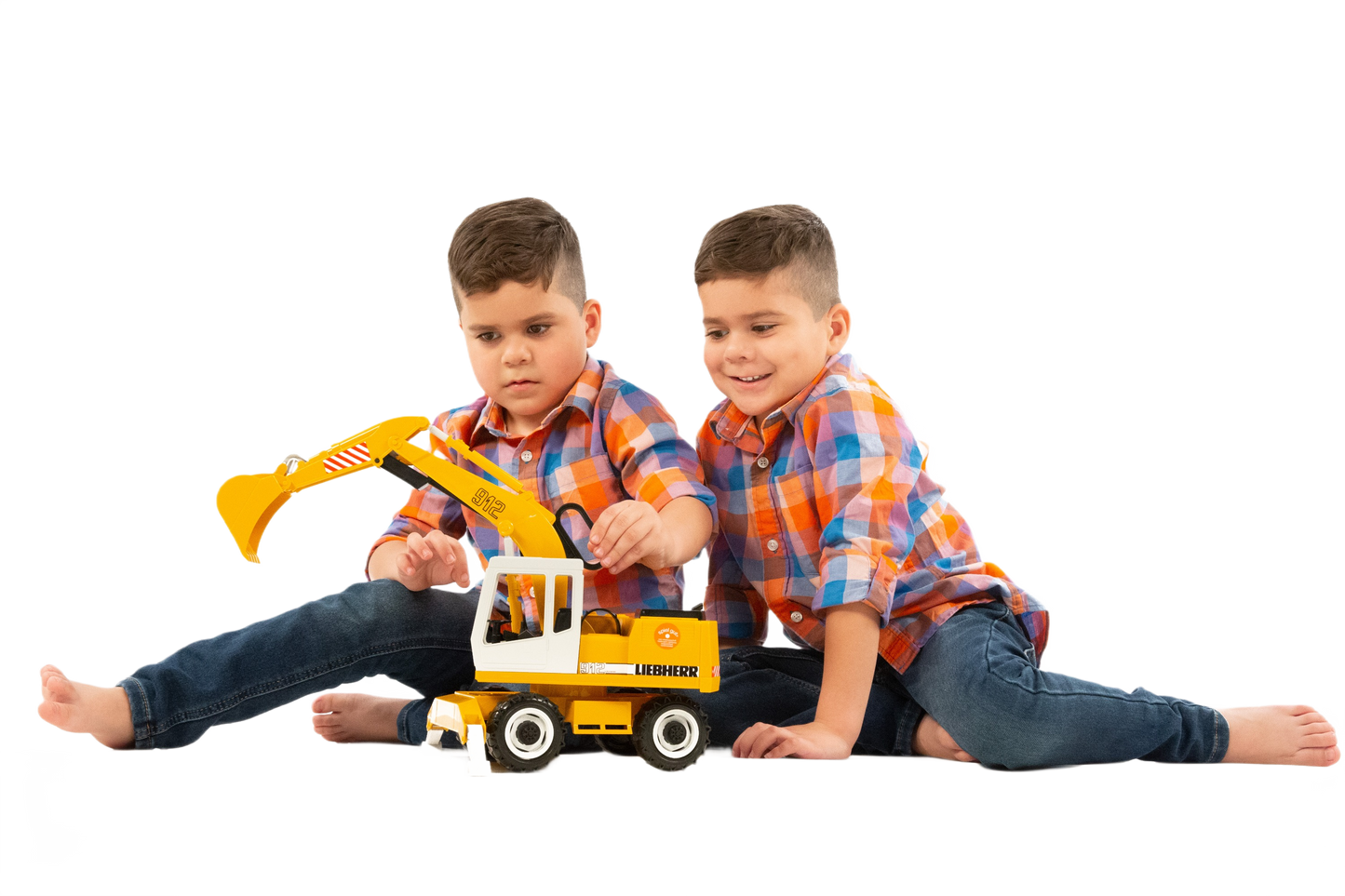 Two young boys in matching plaid shirts playing with a Bruder Liebherr Power Shovel toy from vehicles and toys collections