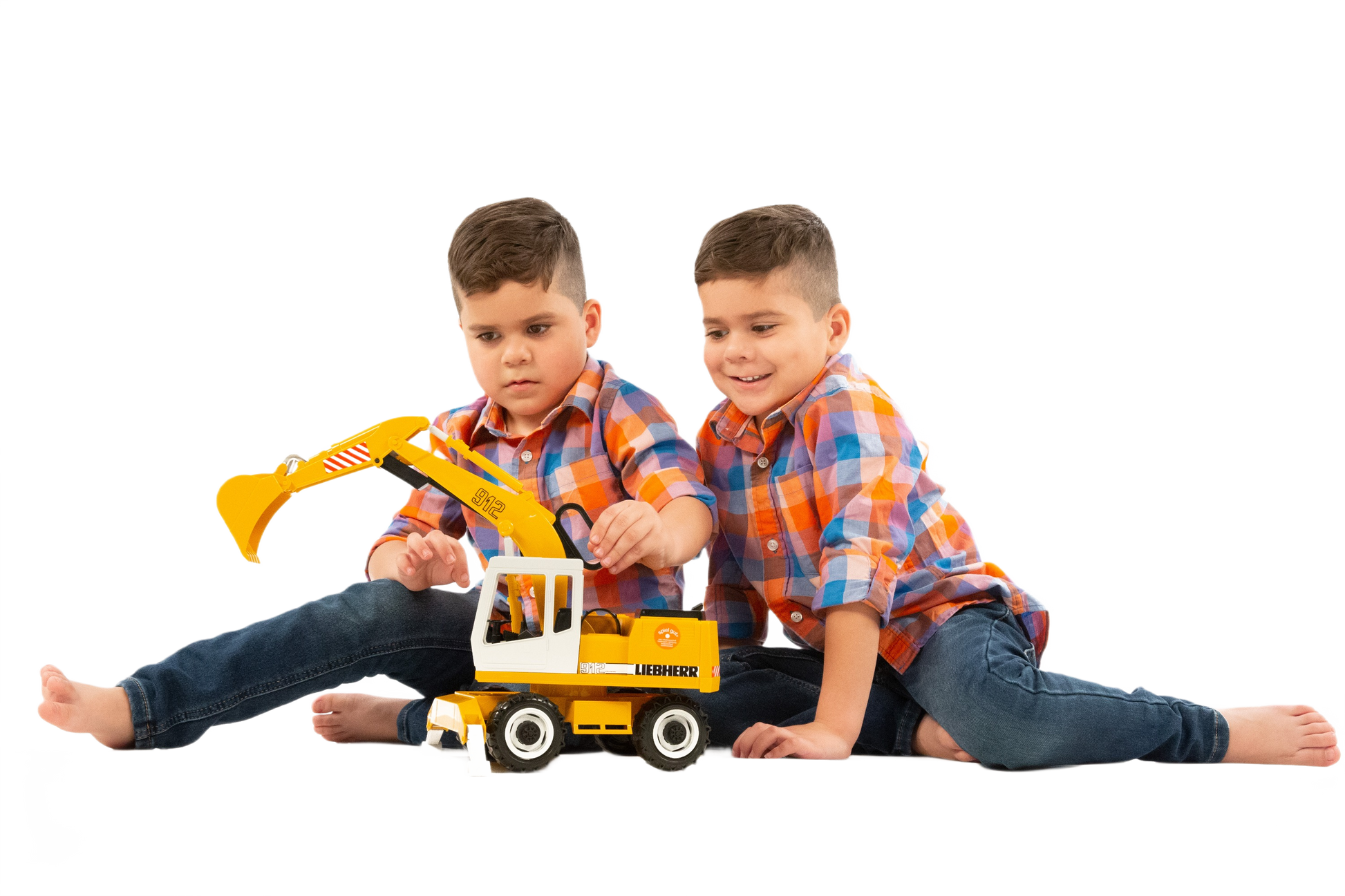 Two young boys in matching plaid shirts playing with a Bruder Liebherr Power Shovel toy from vehicles and toys collections