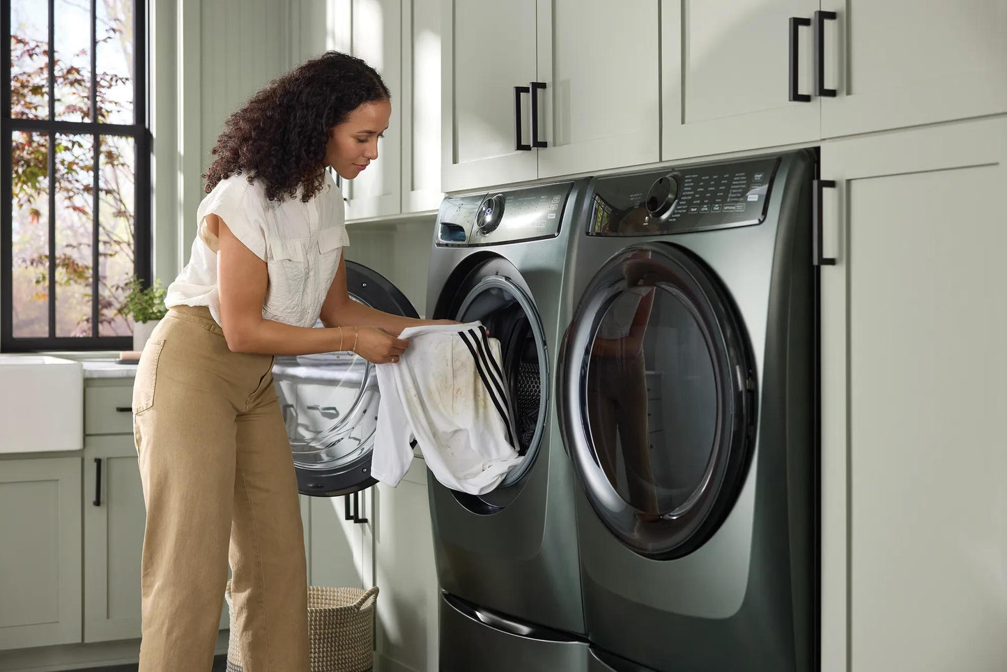 Woman loading white clothes into a dark gray front load washer in a bright laundry room from washers and appliances collection