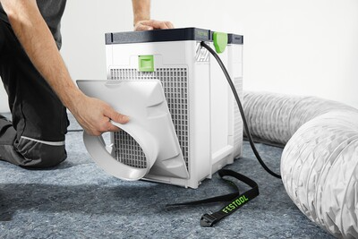 Person attaching flexible dust collection hose to compact portable air filtration unit for woodworking tools usage