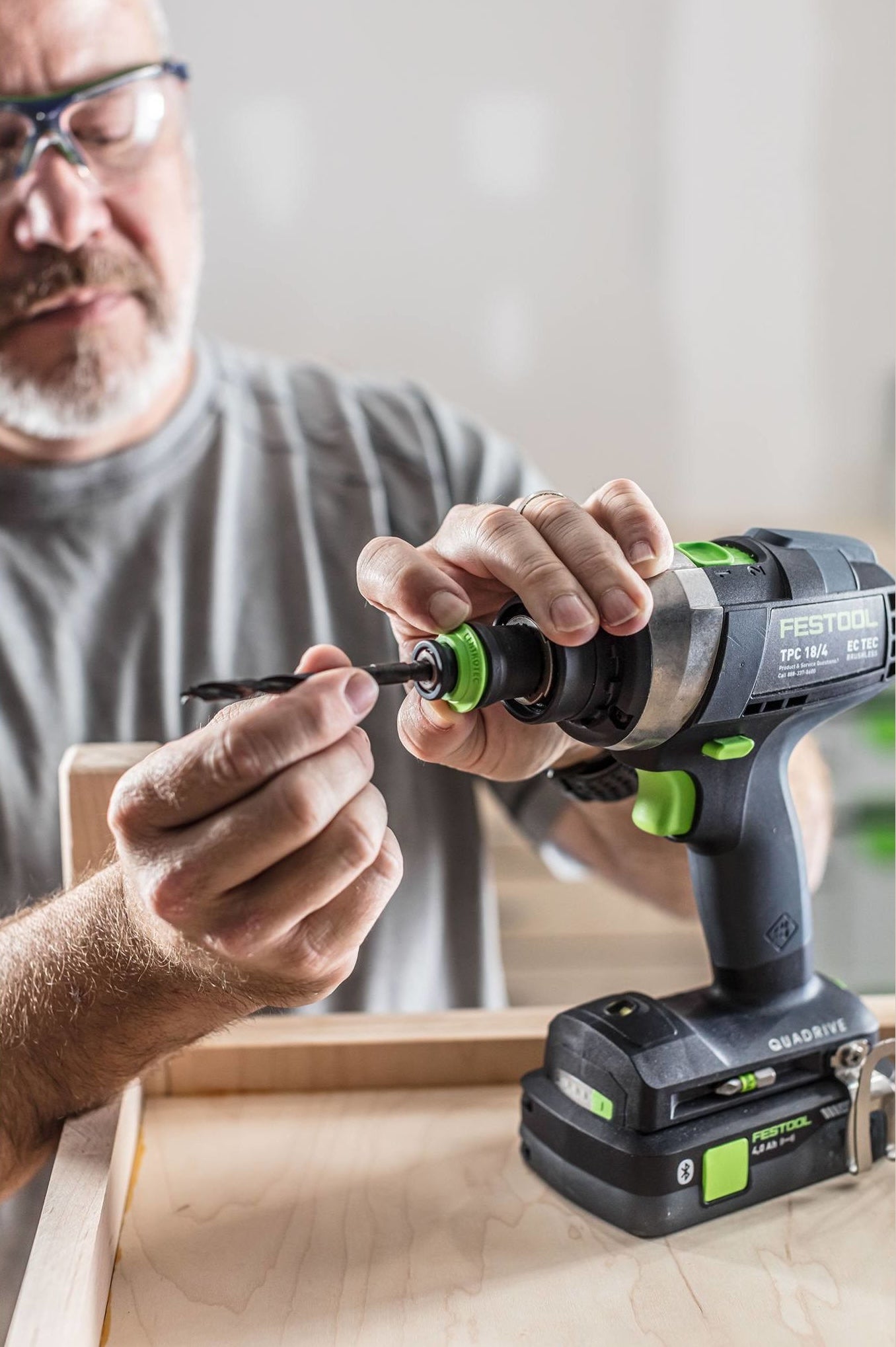 Man wearing safety glasses attaching a drill bit to a Festool power drill for home improvement projects