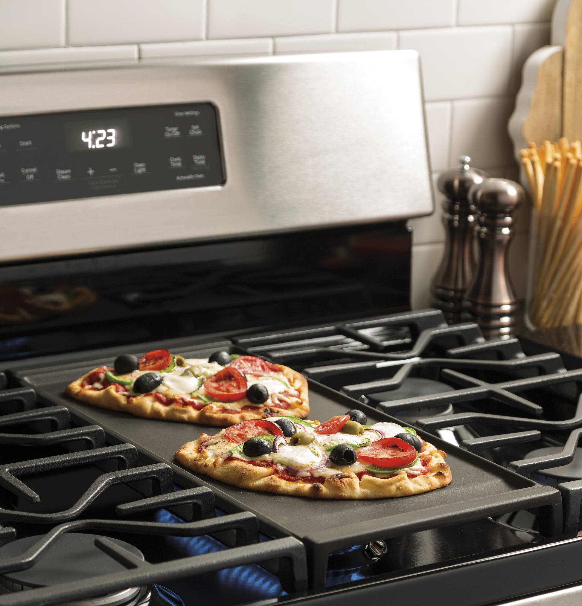 GE 30" gas range with blue flame burners cooking two small vegetable pizzas on a rectangular baking pan