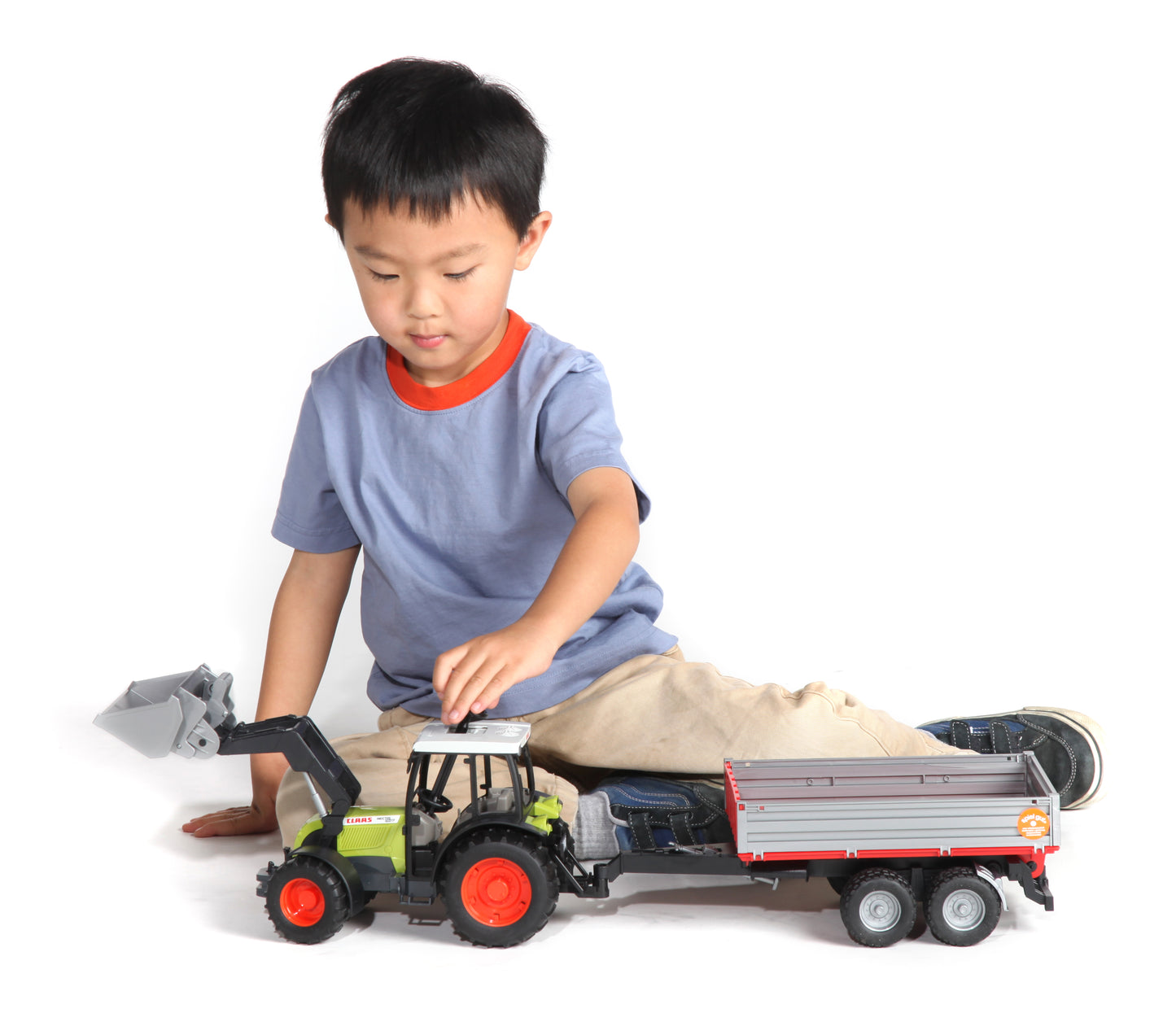 Child playing on floor with green and gray toy tractor and attached red and gray trailer for imaginative play