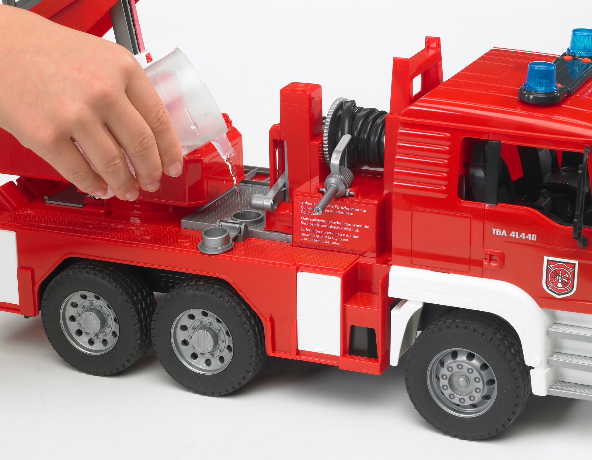 Child pouring water into red Bruder Toys MAN fire engine with ladder, water pump, and detailed features for play collections
