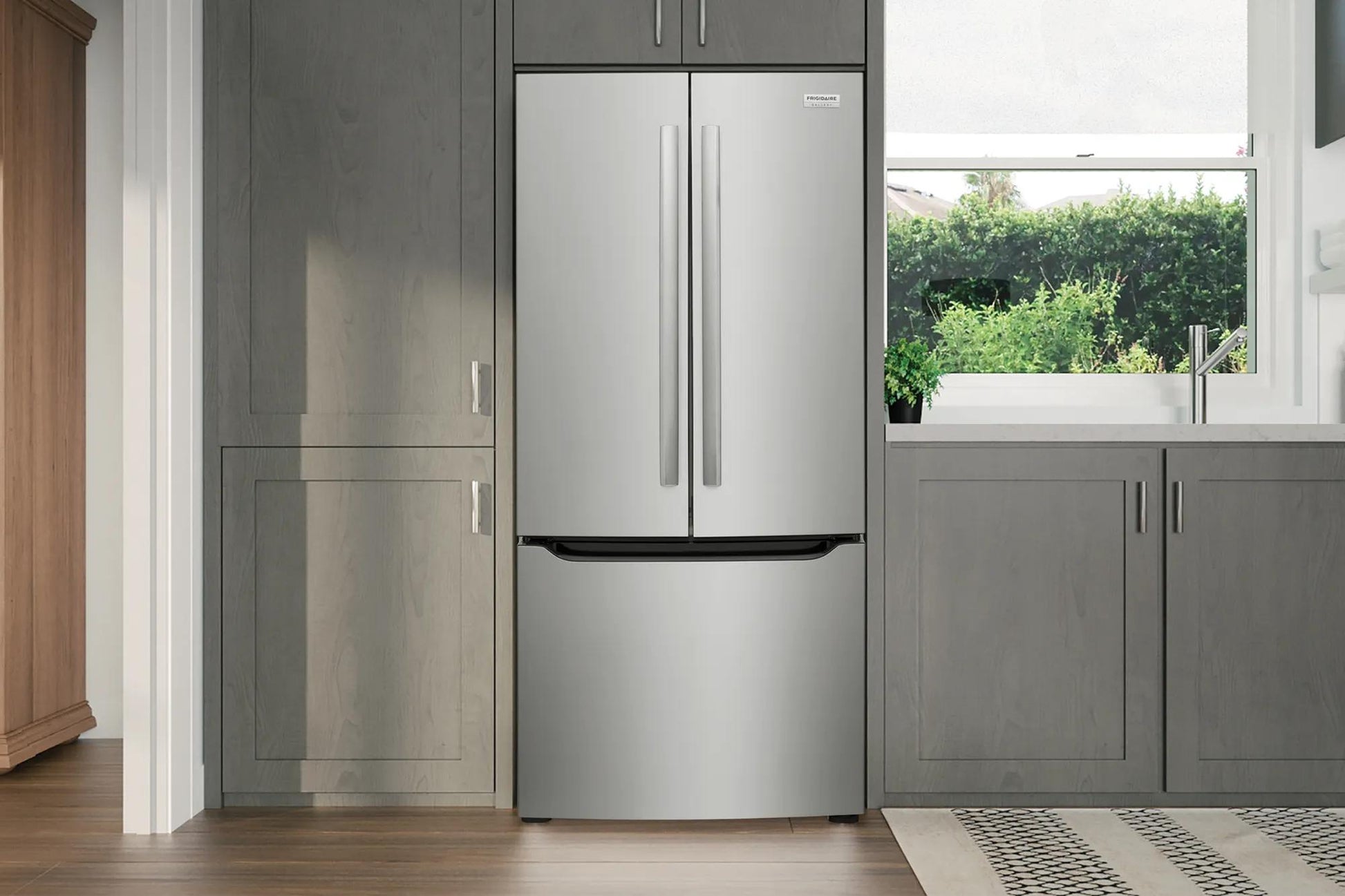 Built-in stainless steel French door refrigerator with bottom freezer in modern kitchen featuring gray cabinetry and window view.