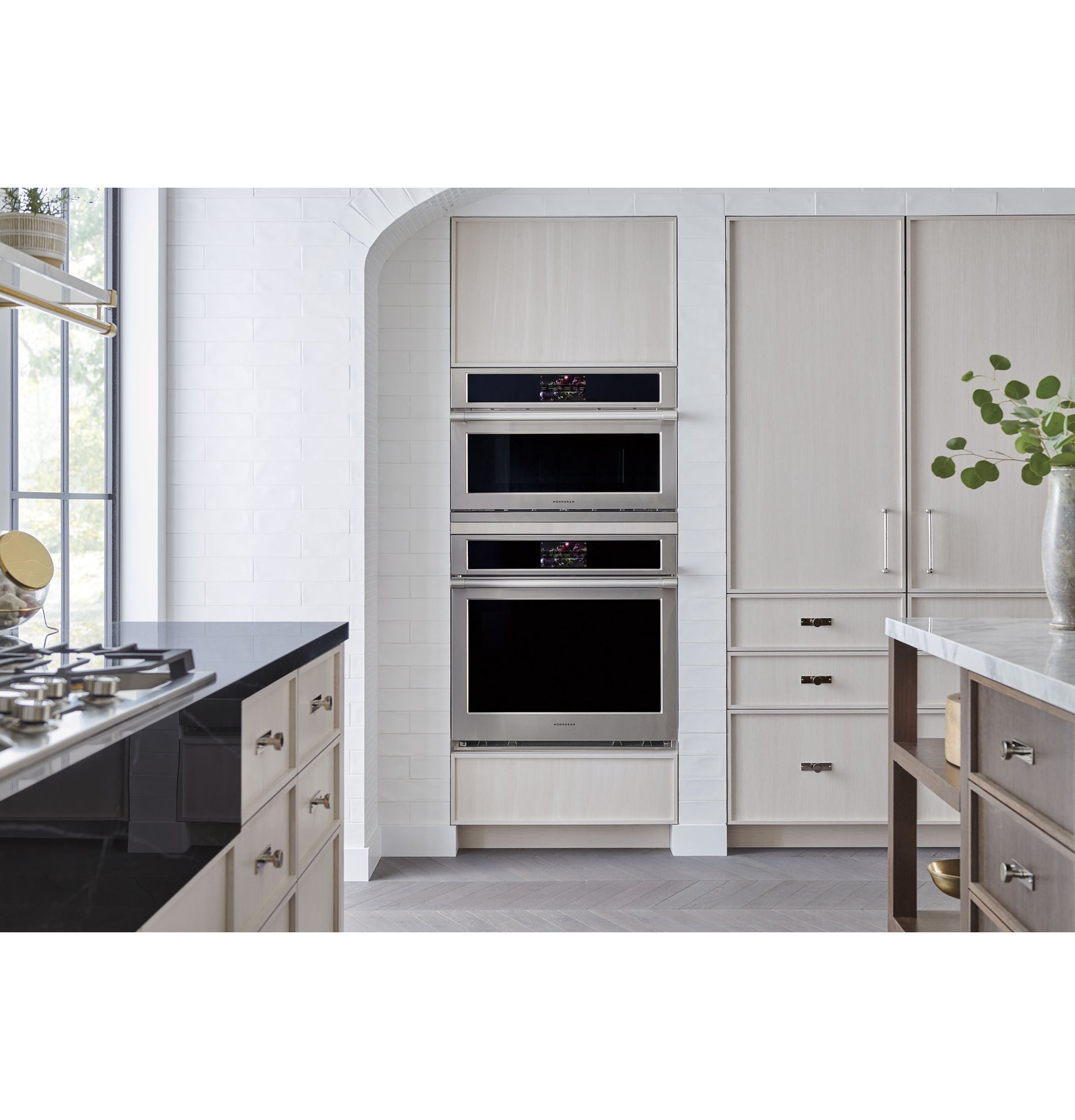 Built-in stainless steel wall oven unit integrated into modern kitchen cabinetry with light wood finishes and a gas cooktop nearby