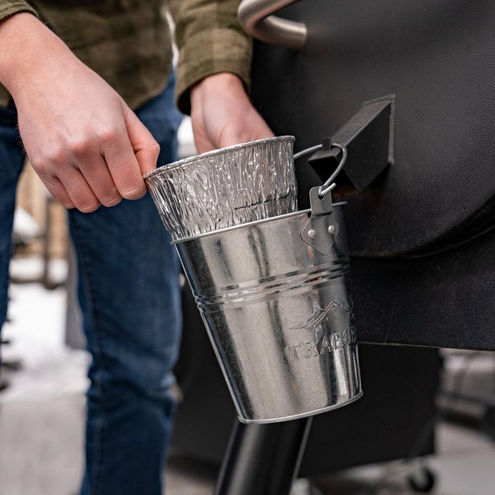 Person placing aluminum grease pan liner into metal bucket on grill for tools and home improvement use