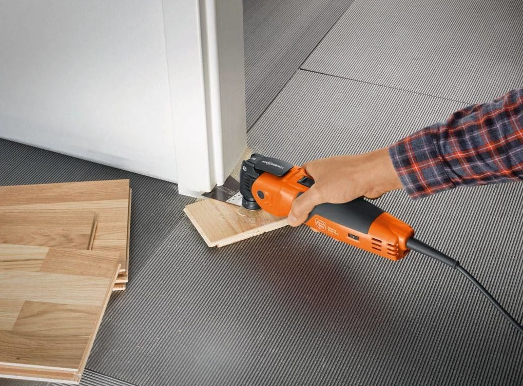 Orange and black oscillating multitool cutting wooden flooring near door frame for home improvement tasks