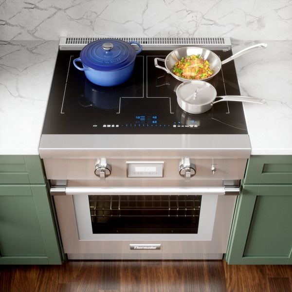 Stainless steel induction range with digital touch controls, cookware on smooth black cooktop in kitchen setting