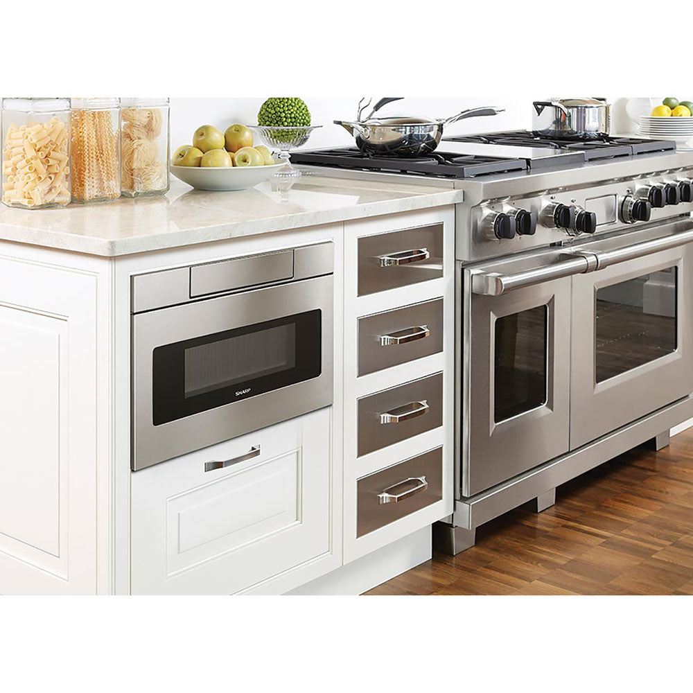 Built-in stainless steel flat panel microwave drawer integrated into white kitchen cabinetry with stove and countertop accessories nearby
