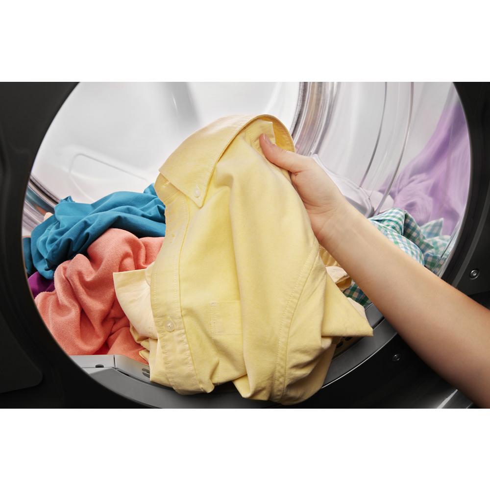 Hand removing yellow shirt from stainless steel front load dryer drum in gas dryers and appliances collection
