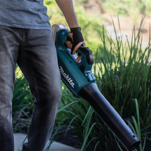 Person using teal Makita cordless blower for outdoor cleaning in home improvement tasks