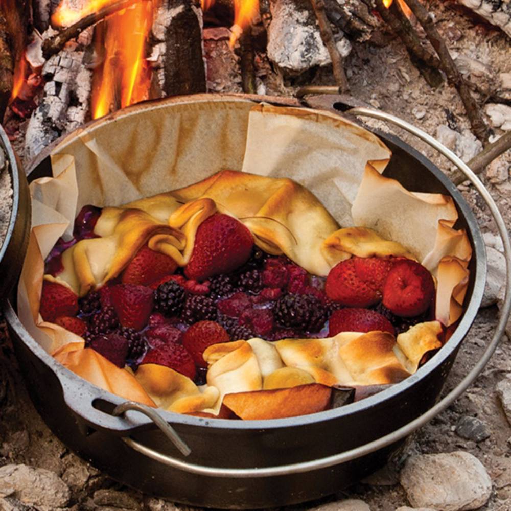 Pre-seasoned Lodge cast iron camp Dutch oven with mixed berry cobbler baking over open campfire outdoors