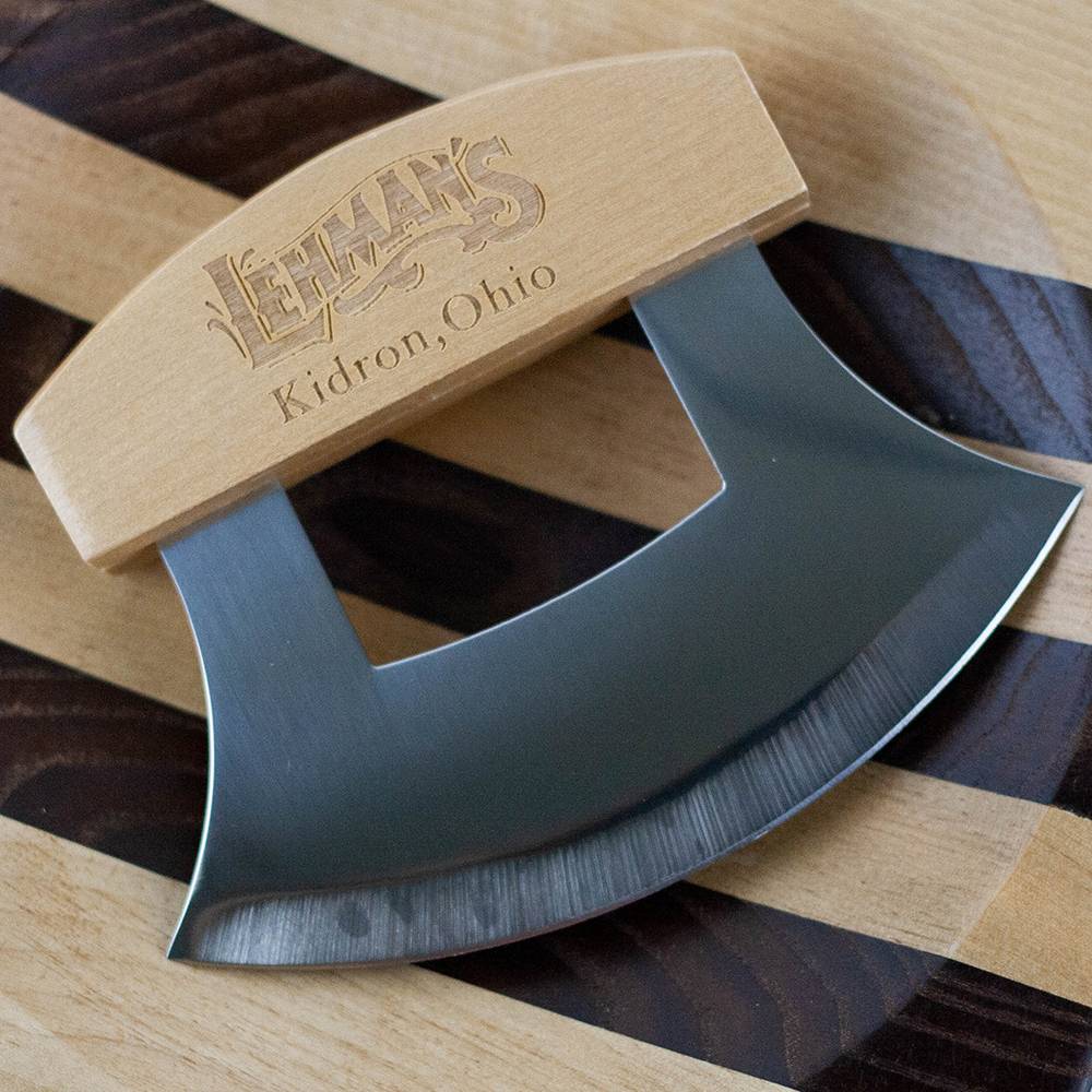 Curved stainless steel ulu knife with wooden handle engraved with Lehman's Kidron Ohio on striped wooden cutting board in kitchenware collection