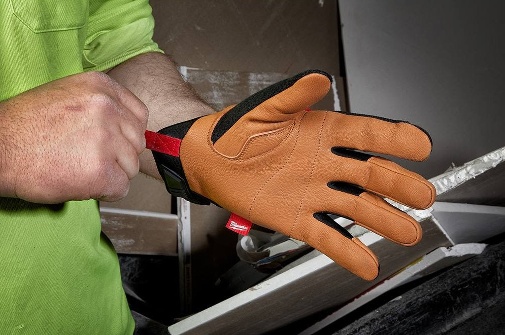 Worker wearing tan leather performance gloves with red and black accents for hardware and safety tasks