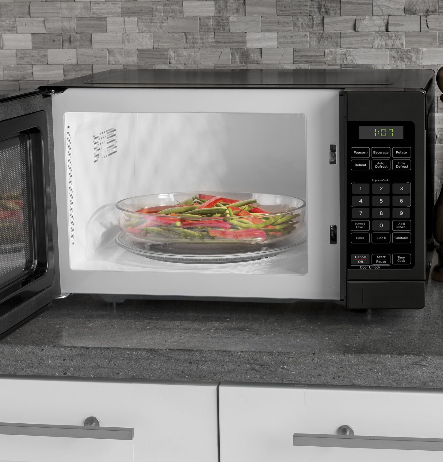 Black countertop microwave with open door, digital control panel, and vegetables on glass turntable inside cooking from Microwaves collection