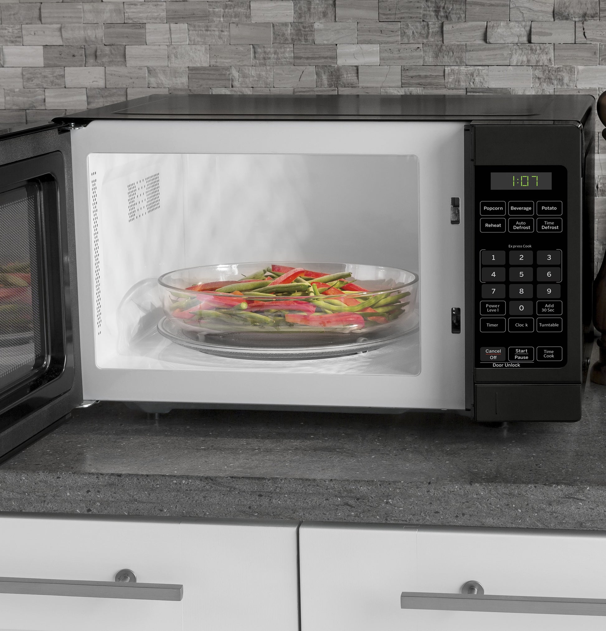 Black countertop microwave with open door, digital control panel, and vegetables on glass turntable inside cooking from Microwaves collection