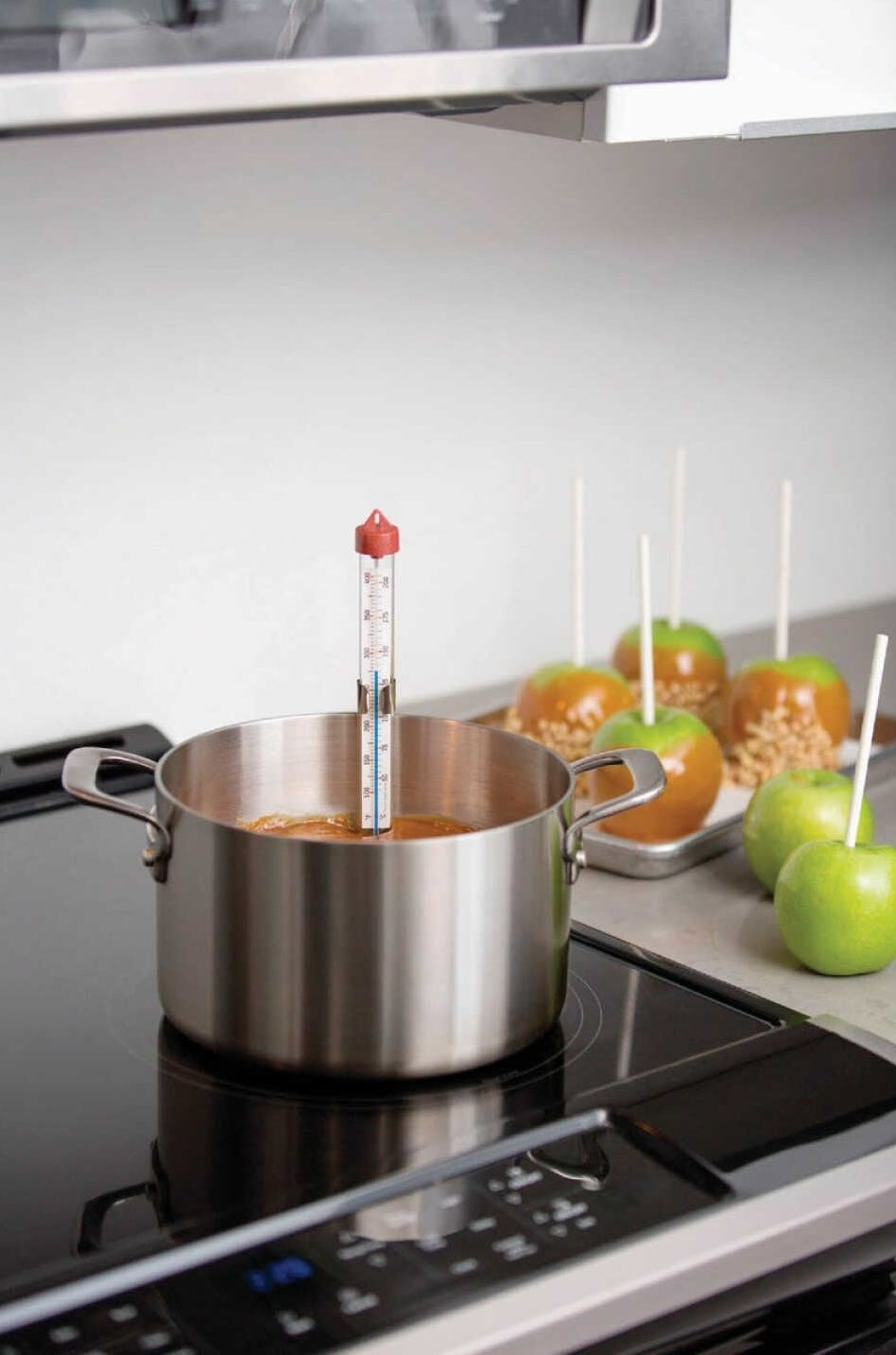 Glass tube thermometer with adjustable clip measuring temperature in stainless steel pot on stove in kitchenware setting