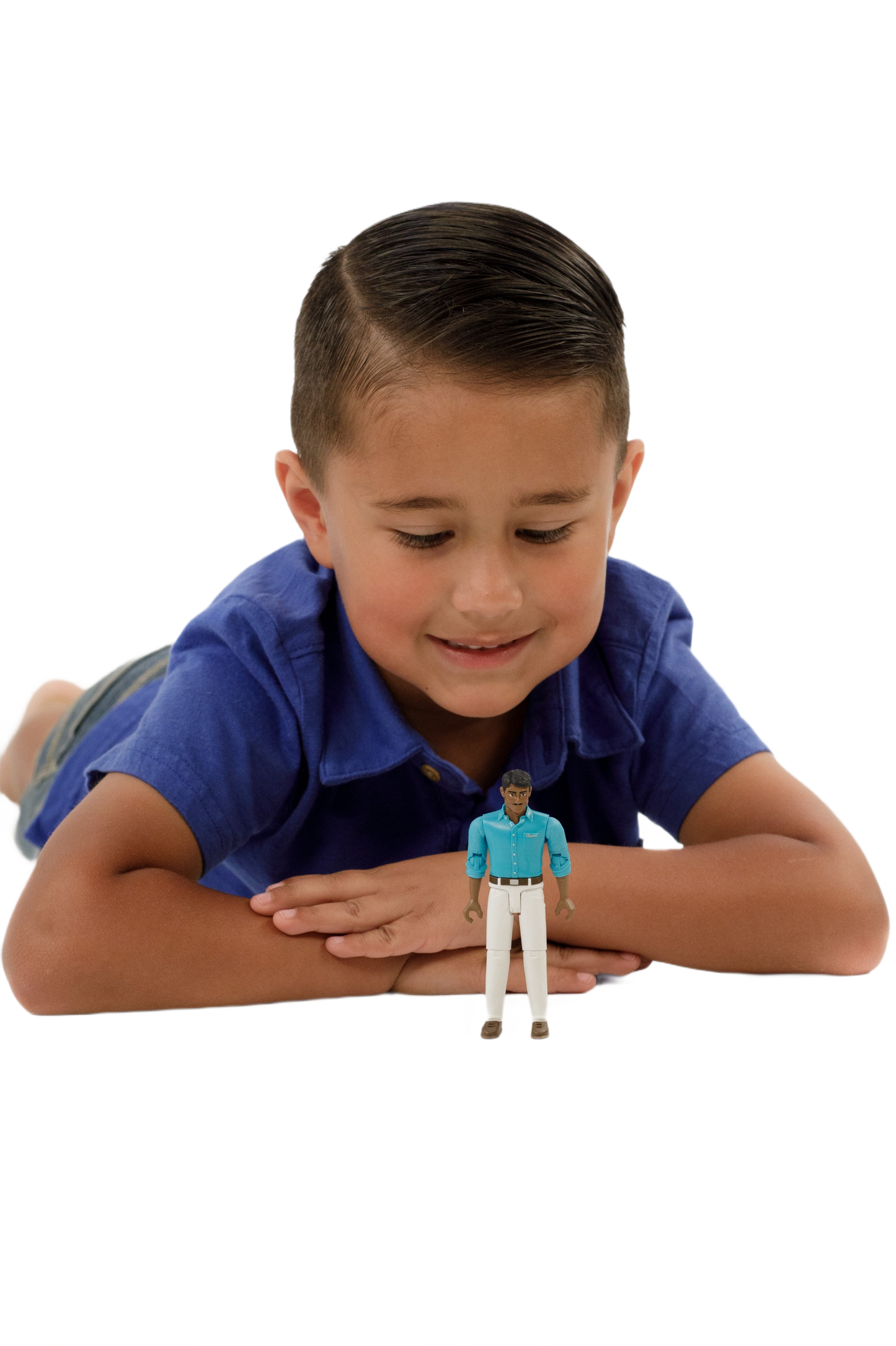 Young boy in blue shirt lying down and smiling at a small action figure wearing teal shirt and white jeans