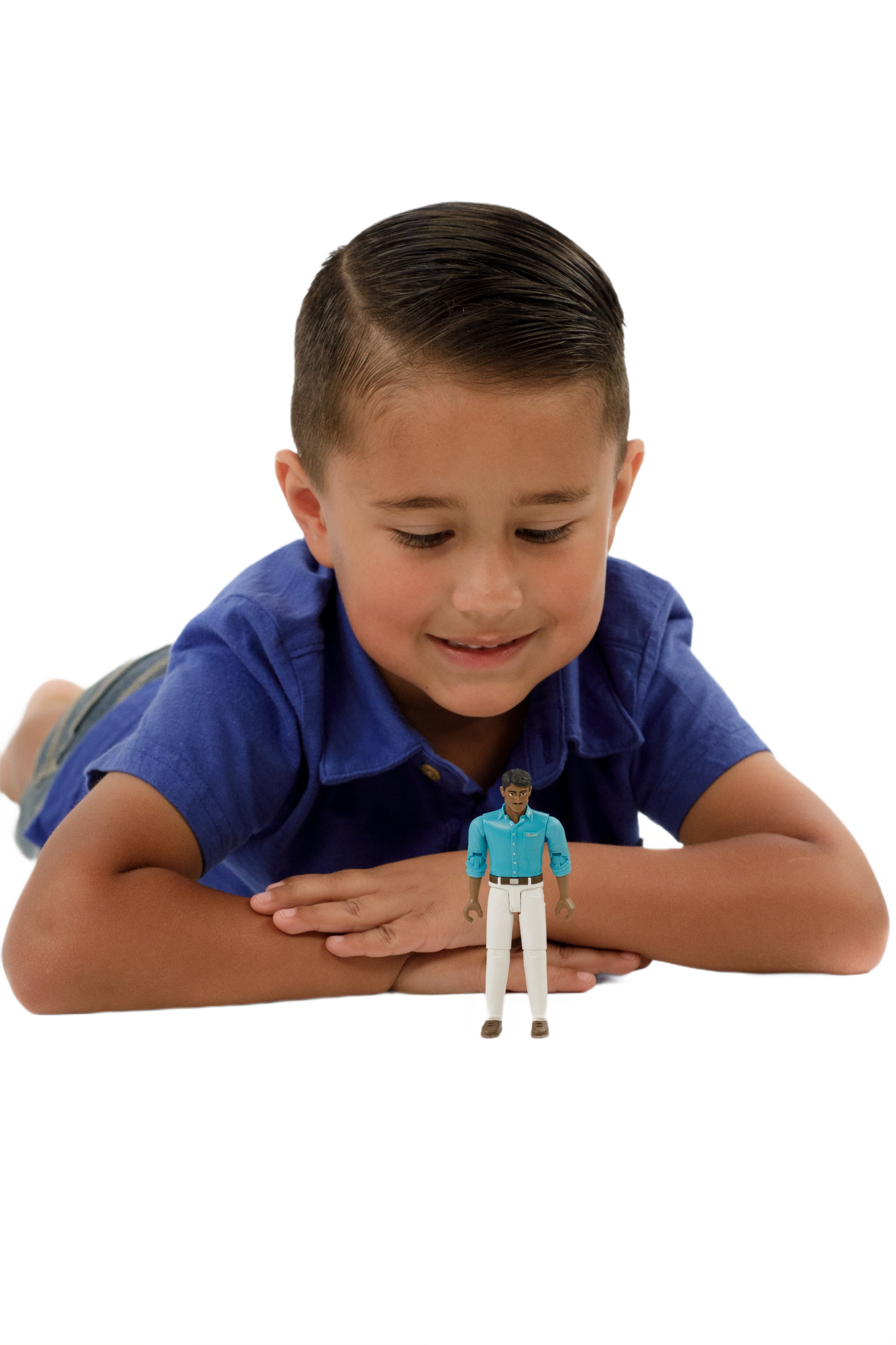 Young boy in blue shirt lying down and smiling at a small action figure wearing teal shirt and white jeans