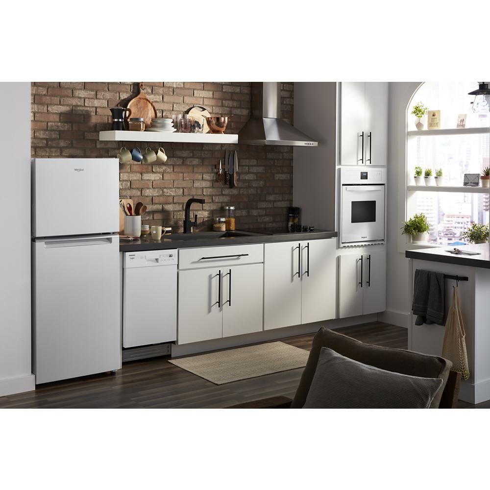 Compact white top-freezer refrigerator in modern kitchen with white cabinetry, brick backsplash, and built-in oven appliances
