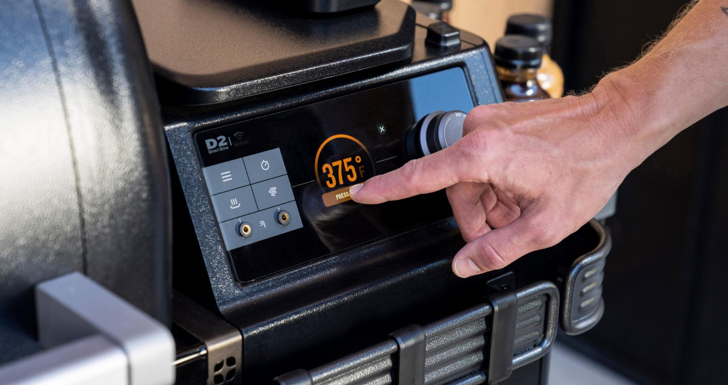 Close-up of a hand adjusting the digital touchscreen on a Traeger IronWood XL WiFire pellet grill in outdoor living setup