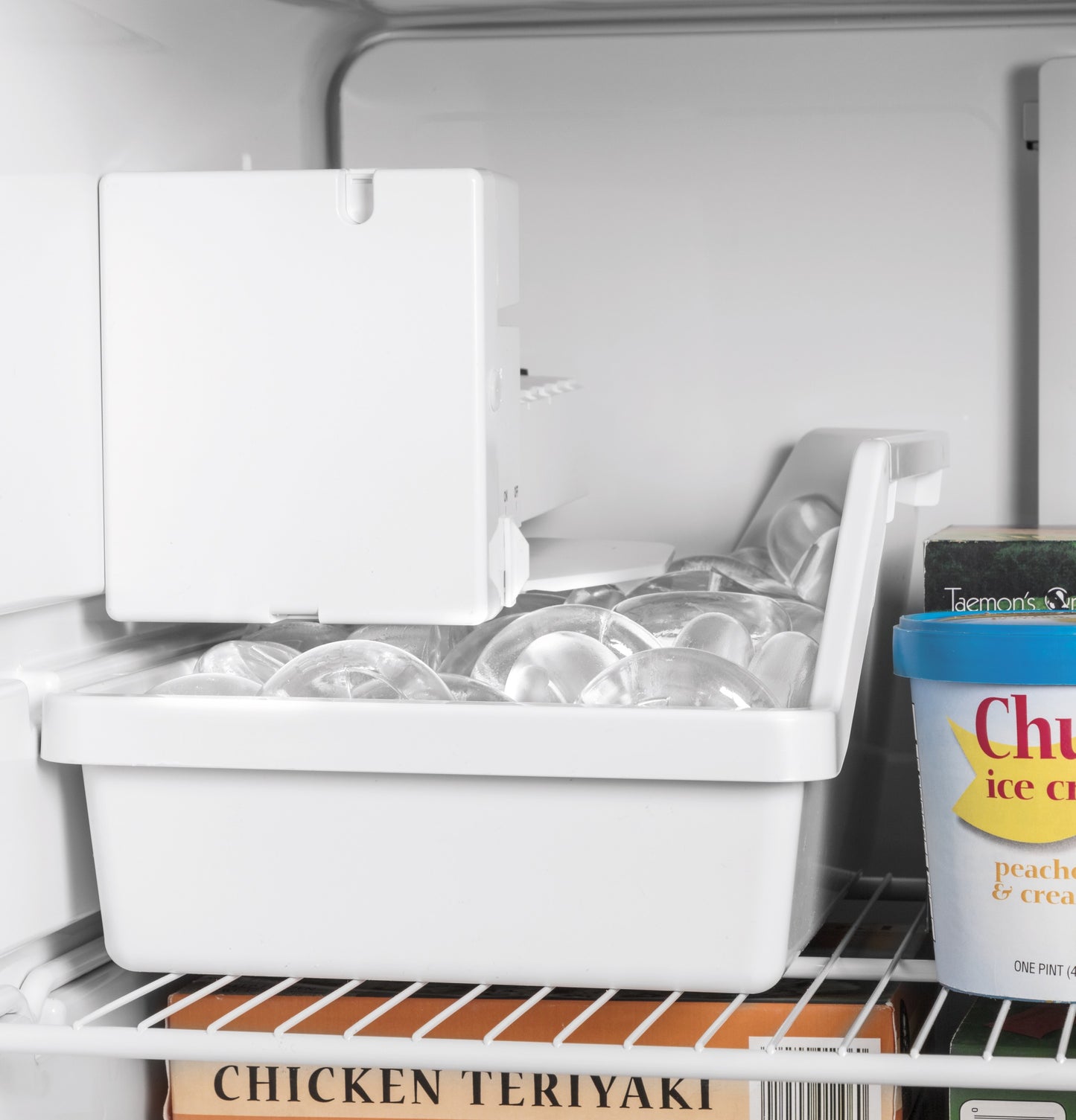 Inside view of top freezer refrigerator showing ice cube tray with clear ice and frozen food containers
