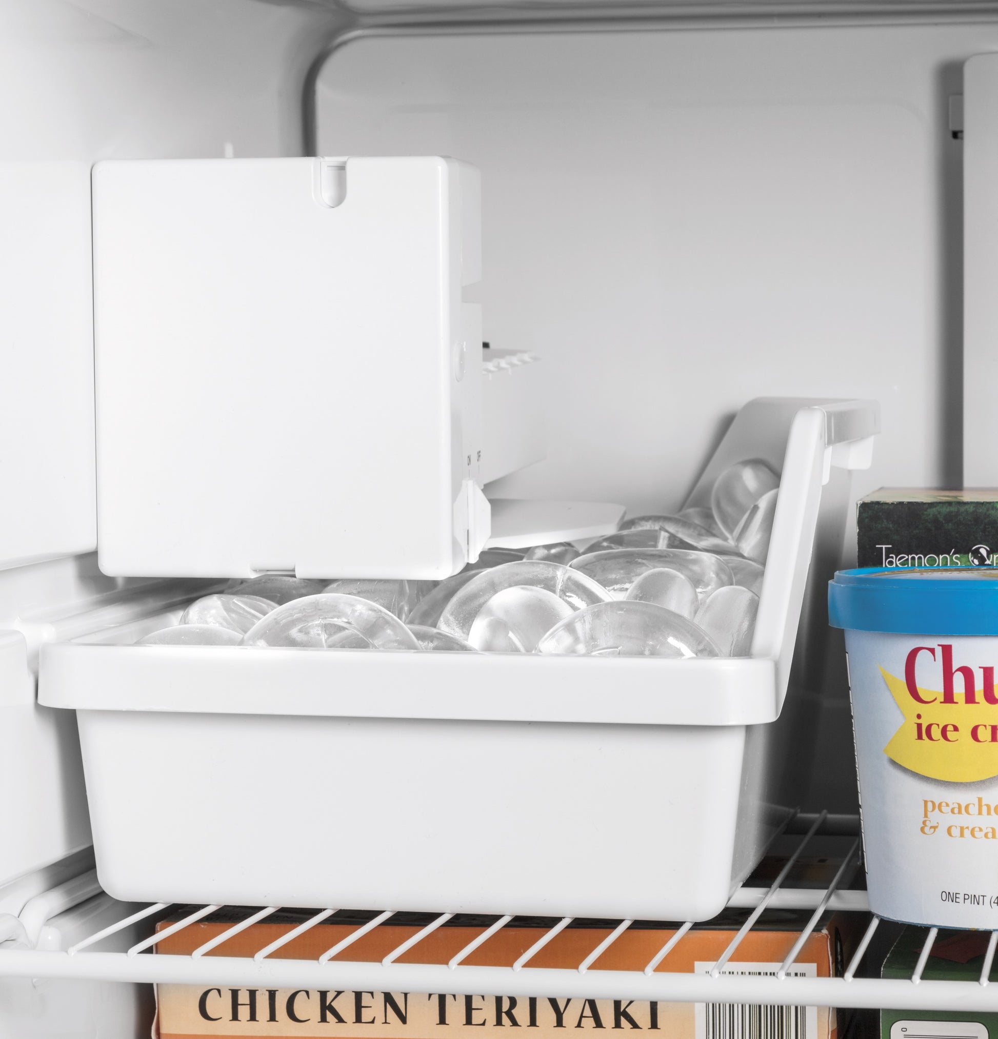 Inside view of top freezer refrigerator showing ice cube tray with clear ice and frozen food containers