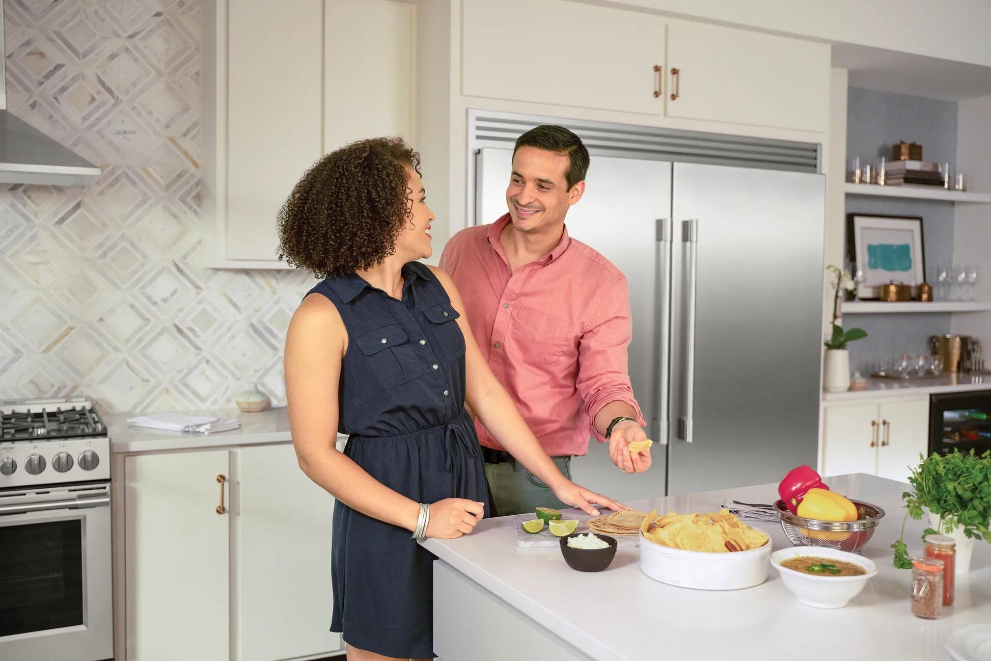 Couple enjoying snacks at kitchen island with stainless steel double-door refrigerator in modern kitchen setting