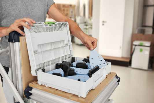 Person handling light blue abrasives organized in gray Festool Systainer for sanding accessories and power tools