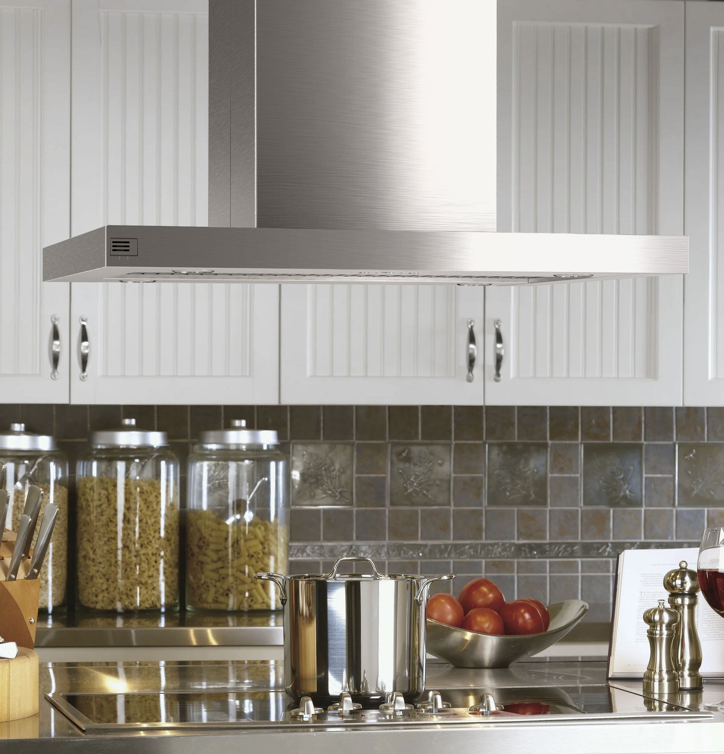 Stainless steel island-mount vent hood above cooktop with cookware and kitchenware in modern kitchen setting