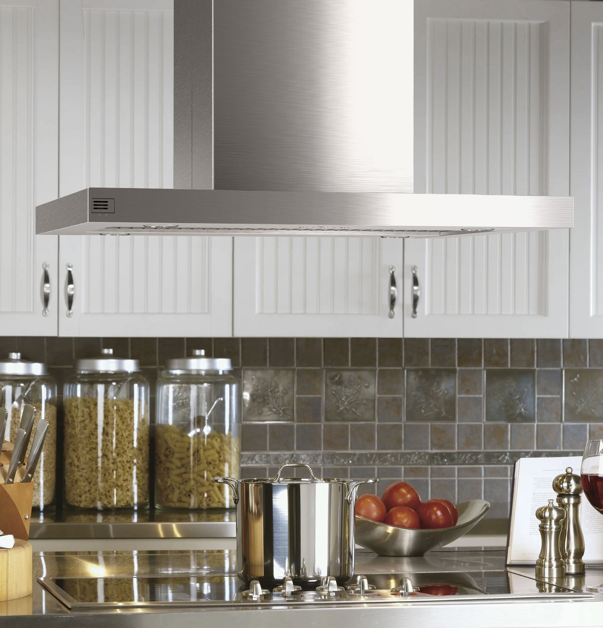 Stainless steel island-mount vent hood above cooktop with cookware and kitchenware in modern kitchen setting