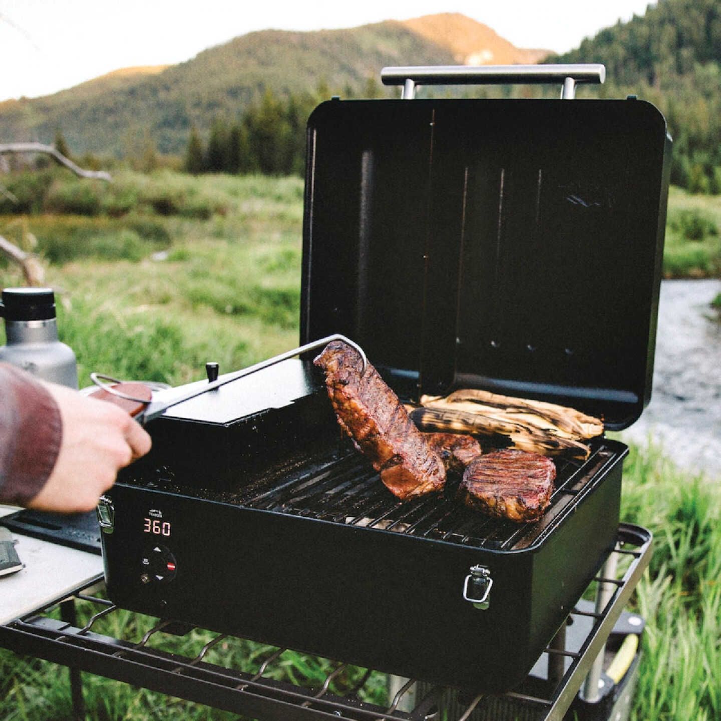 Outdoor black portable pellet grill with digital temperature display cooking steaks and vegetables in nature setting