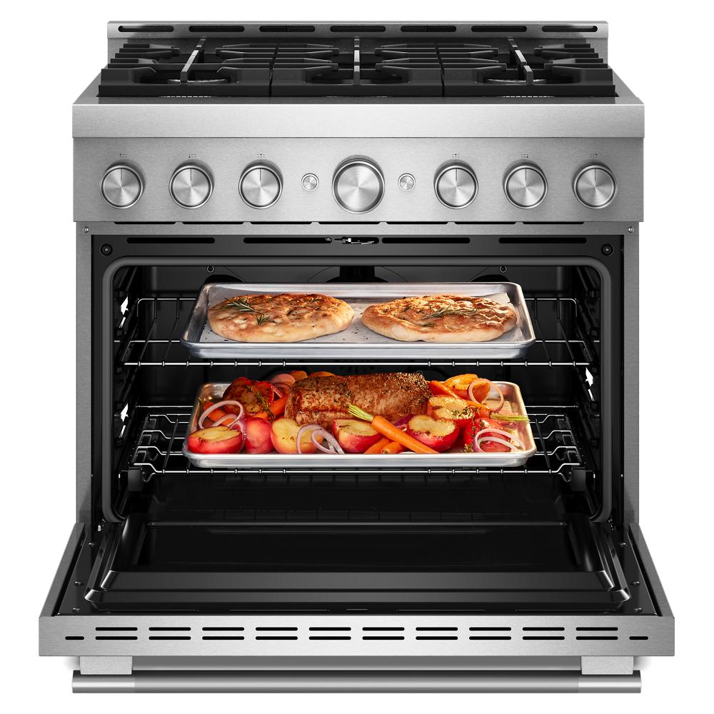Stainless steel gas range with six burners and open oven showing baking trays with roasted meat and pizza inside.