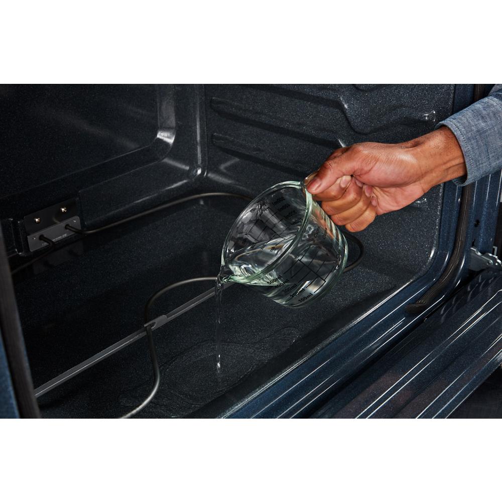 Hand pouring water into oven interior to prepare steam cleaning cycle for home kitchen appliance maintenance