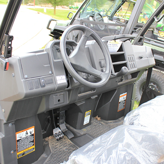 Interior view of utility vehicle dashboard featuring steering wheel, pedals, and control switches in rugged cabin