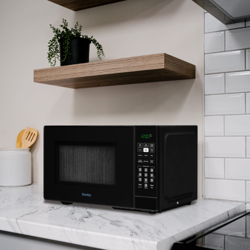 Black countertop microwave with keypad controls and green digital timer on marble kitchen counter near wooden shelf