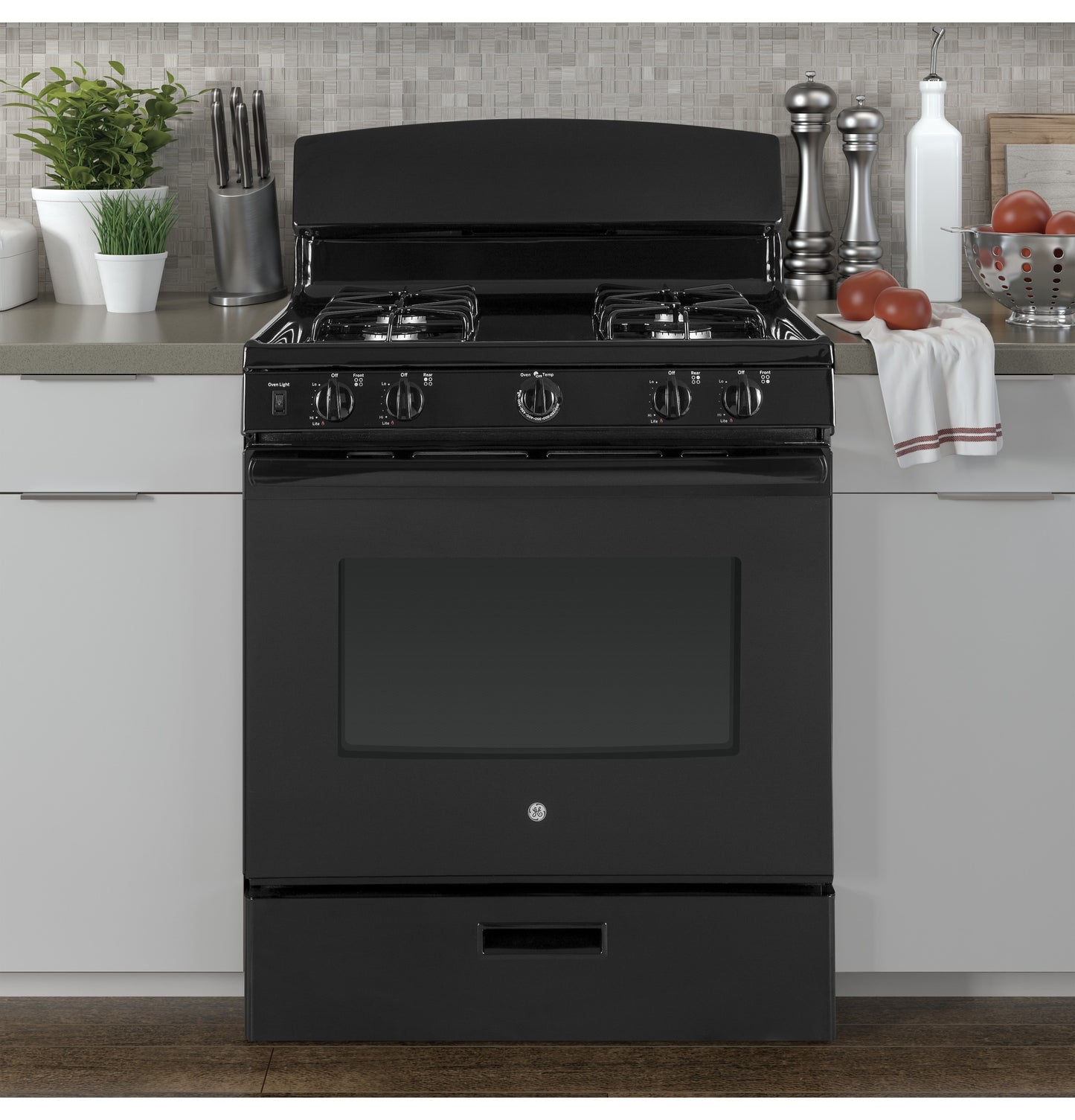 Black free-standing gas range with four burners in modern kitchen setting with countertop decor and backsplash tiles