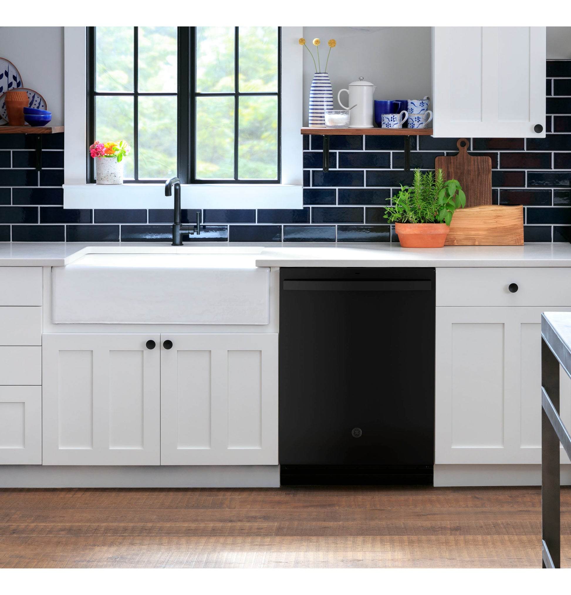 Black top control dishwasher integrated into white cabinetry in modern kitchen with black tile backsplash and farmhouse sink