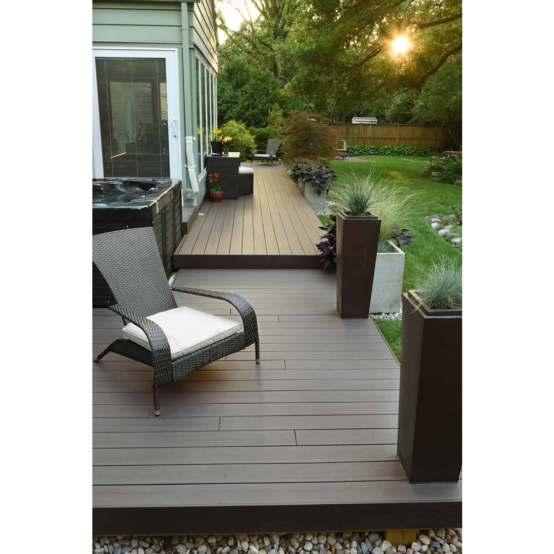 Outdoor deck with espresso-colored composite riser board, modern chair, and planters in a landscaped backyard setting
