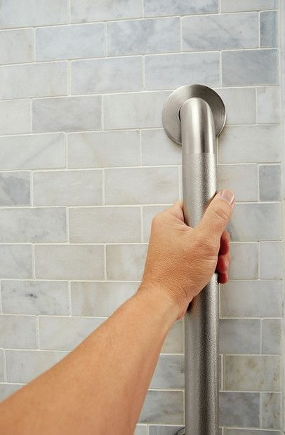 Hand gripping a textured stainless steel grab bar with concealed mounting on tiled bathroom wall for safety support
