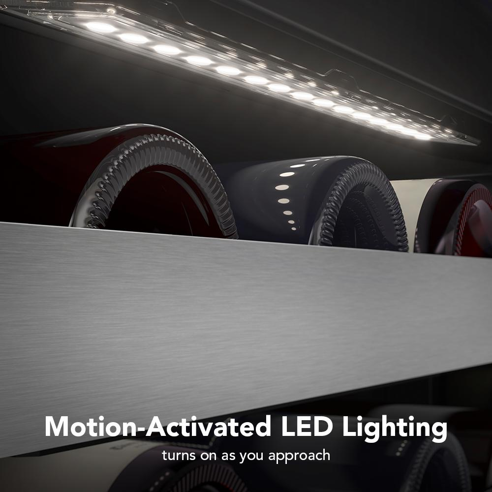 Close-up of motion-activated LED light illuminating wine bottles on metal-front racks inside undercounter wine cellar.