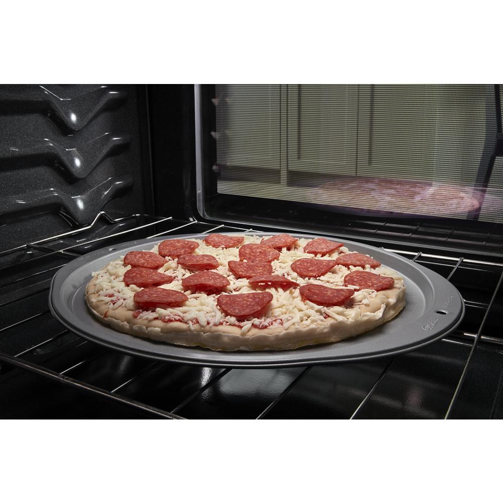 Pepperoni pizza on baking pan inside an electric oven with visible oven racks and textured interior walls