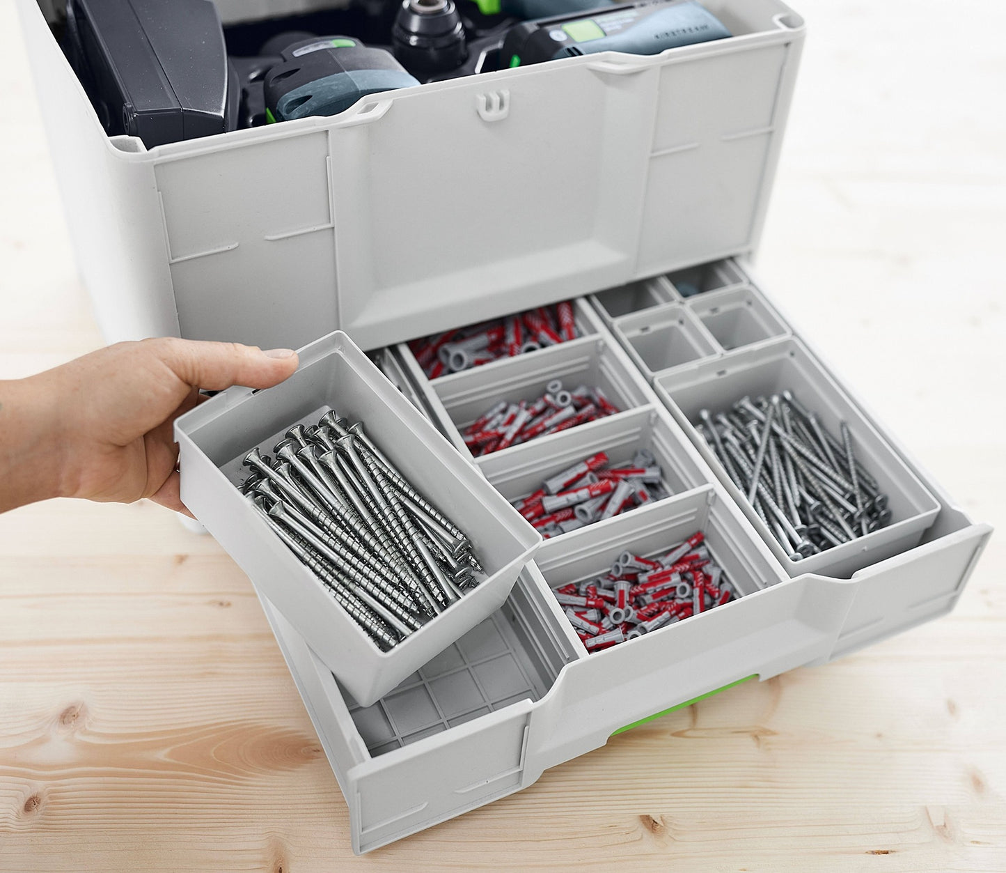 Gray plastic organizer drawer with compartments holding screws and wall anchors, part of a modular tool storage system for workshop organization.