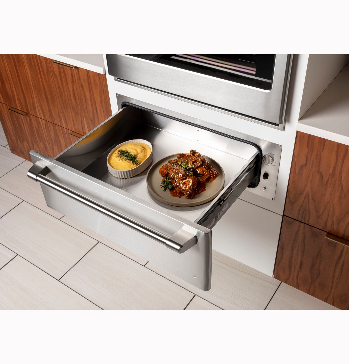 Stainless steel warming drawer with open front in modern kitchen, heating plated food from wall ovens collection
