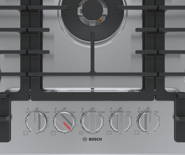 Close-up of stainless steel gas cooktop controls with five burner knobs and black cast iron grates from Bosch collection