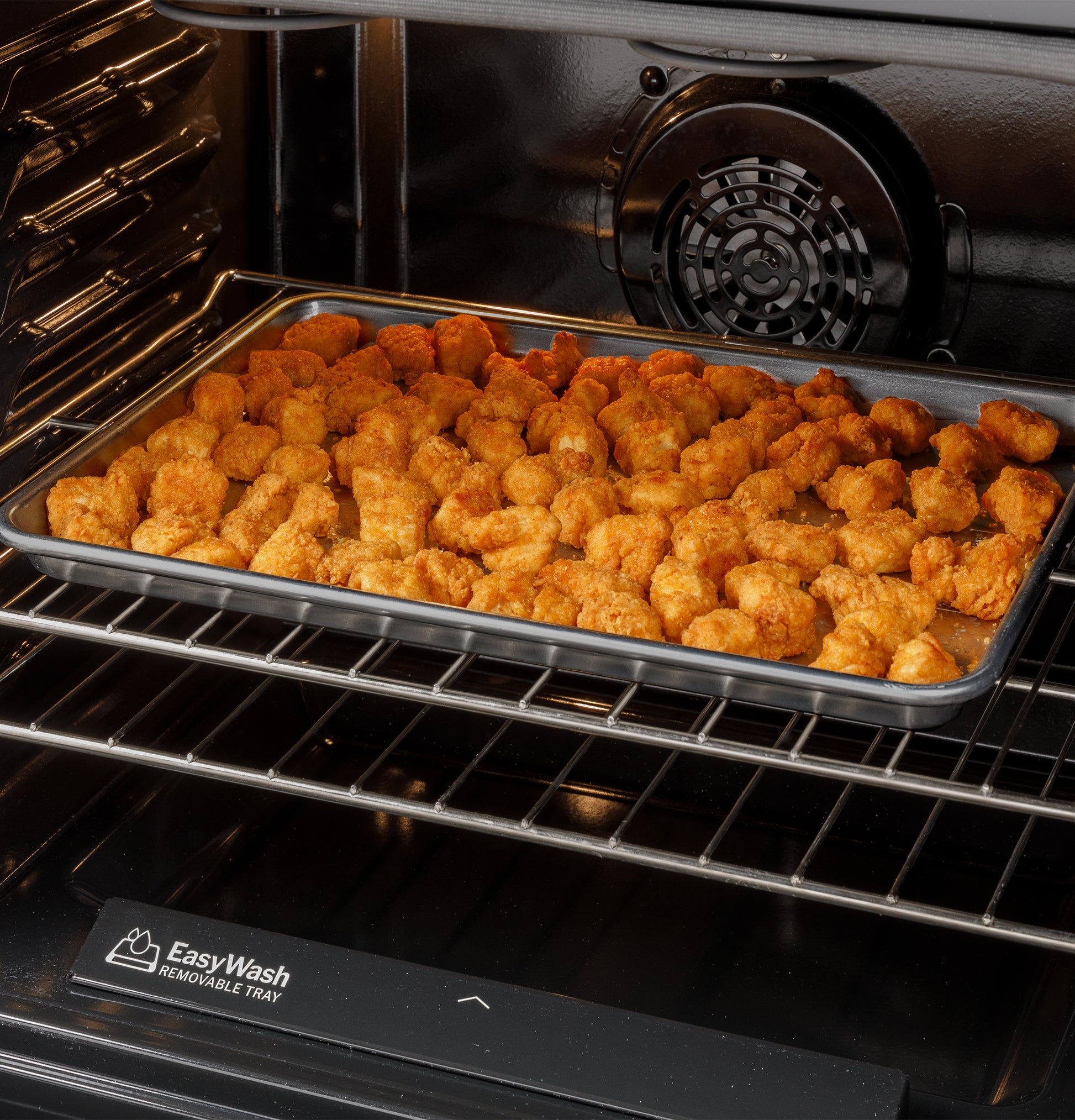 Tray of golden tater tots cooking on oven rack inside a black convection range from Ranges & Cooktops collection